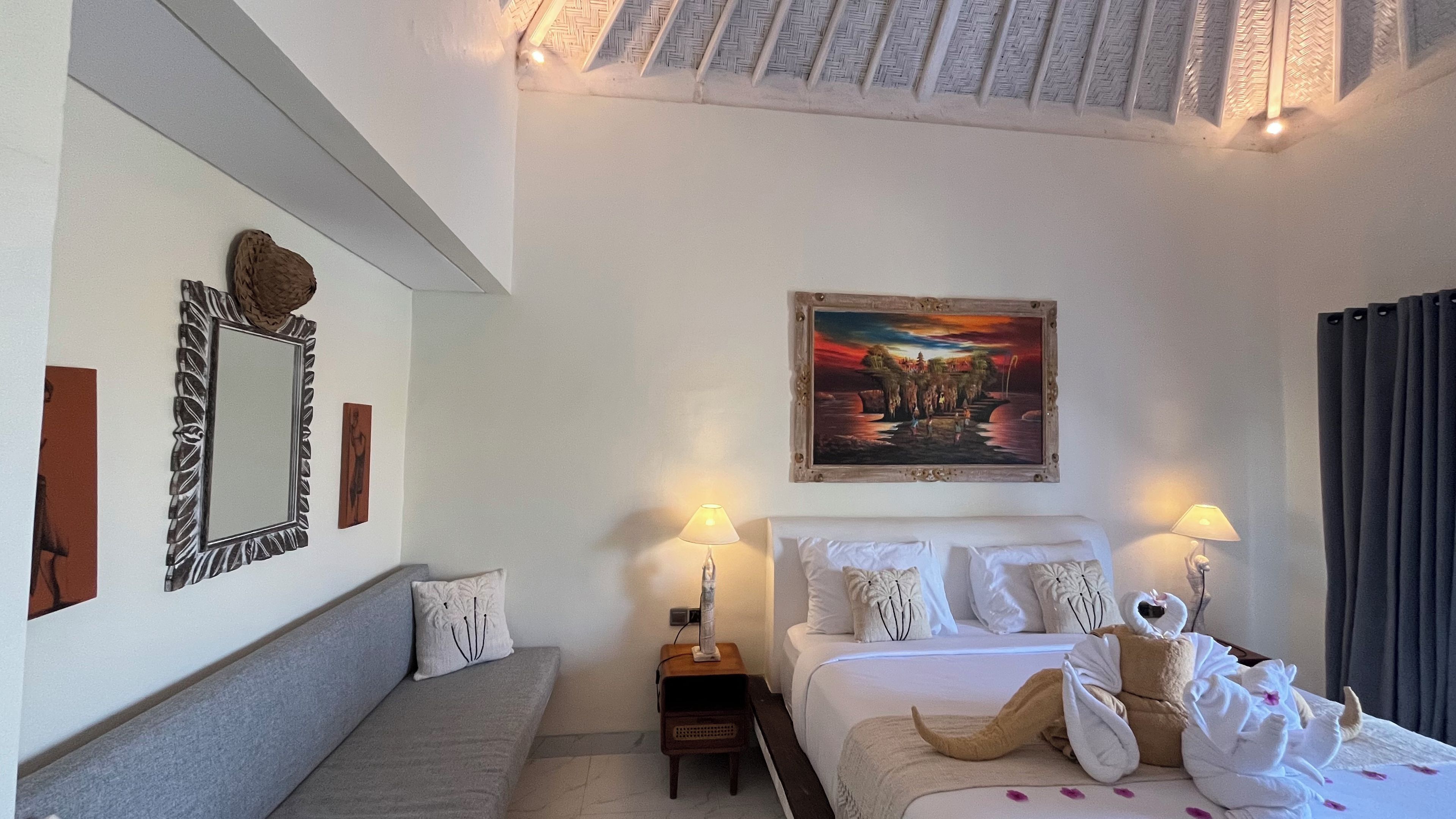 A hotel room with a bed, bedside tables, a sofa, a painting, and a mirror.