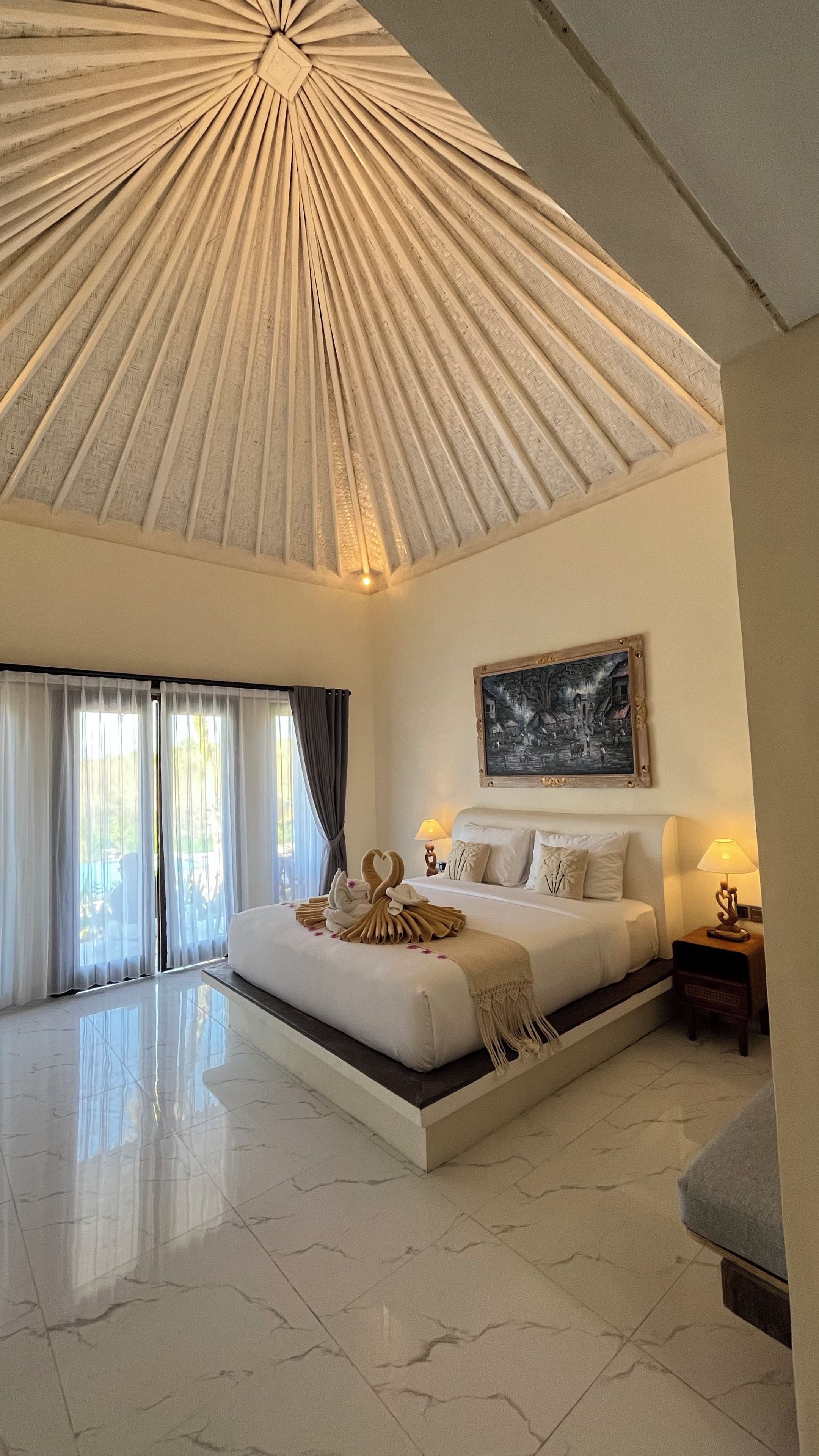A spacious bedroom with a large bed, a ceiling with a radial design, and a painting on the wall.
