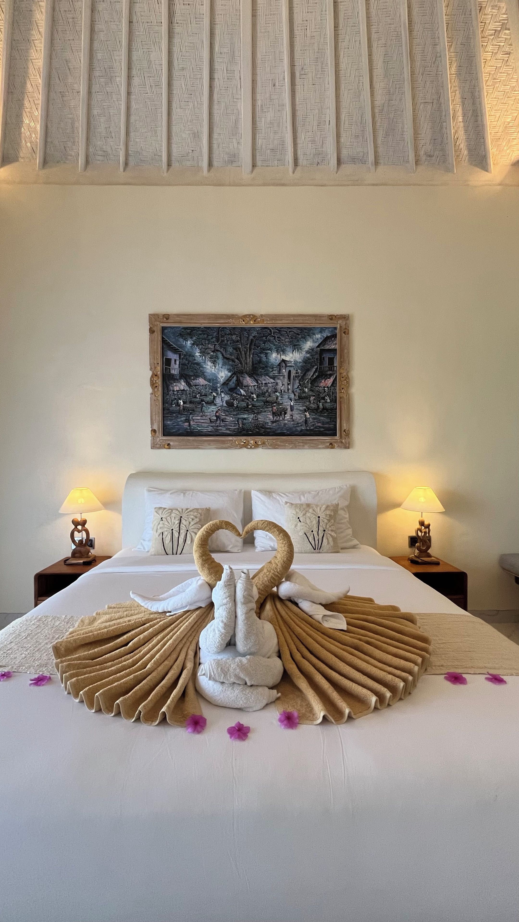 Une chambre d’hôtel avec un lit, deux tables de chevet, un tableau au-dessus du lit et une présentation originale des serviettes.