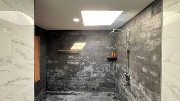 A shower area with a stone wall, a ceiling light, and a shelf with toiletries.