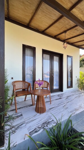 A covered outdoor seating area with two wooden chairs and a table, a wooden ceiling, and a tiled floor. - The Hills Penida (Klungkung)
