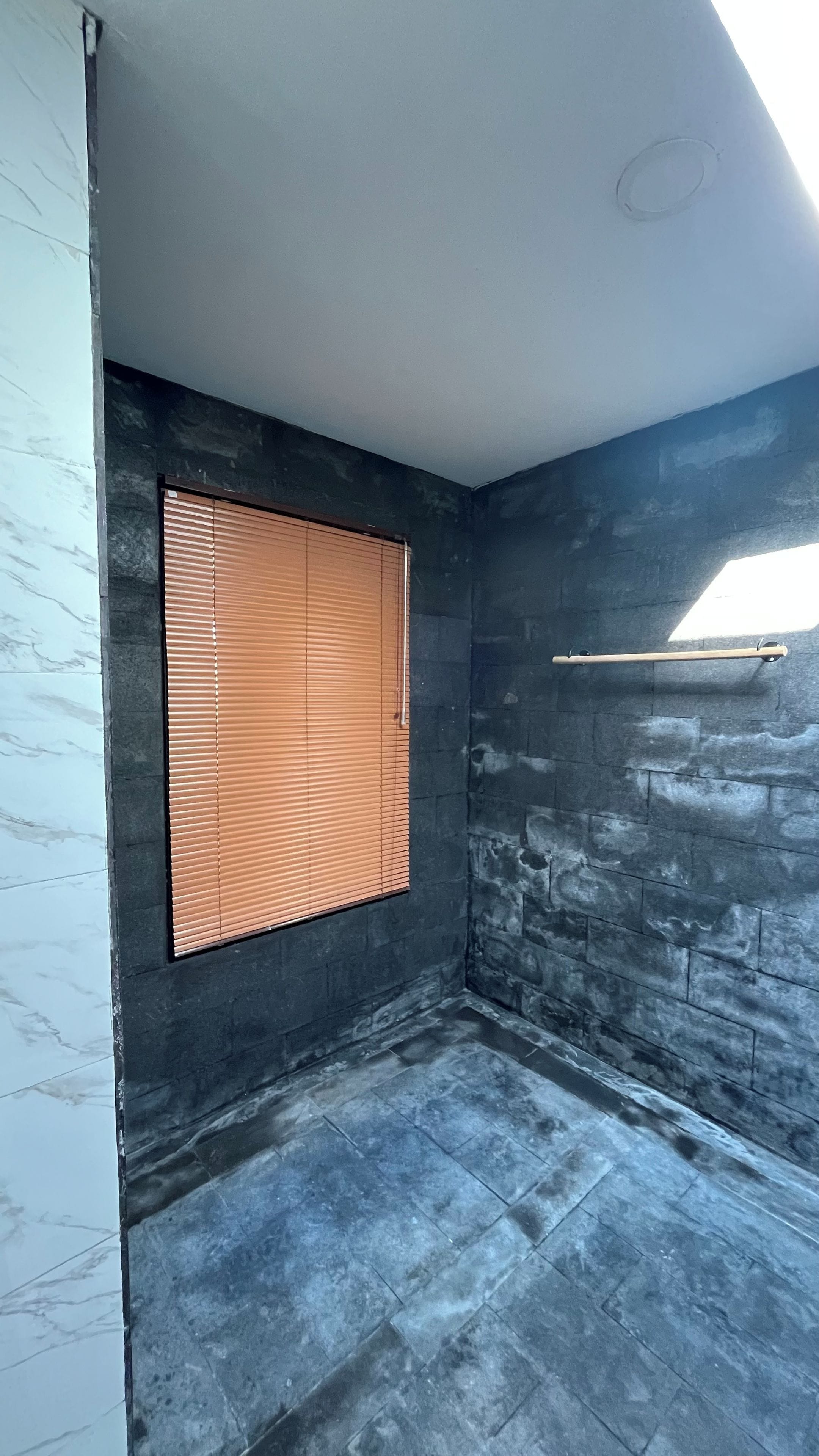 A room with a stone wall, a window with blinds, and a ceiling with a skylight.