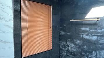 A room with a stone wall, a window with blinds, and a ceiling with a skylight.