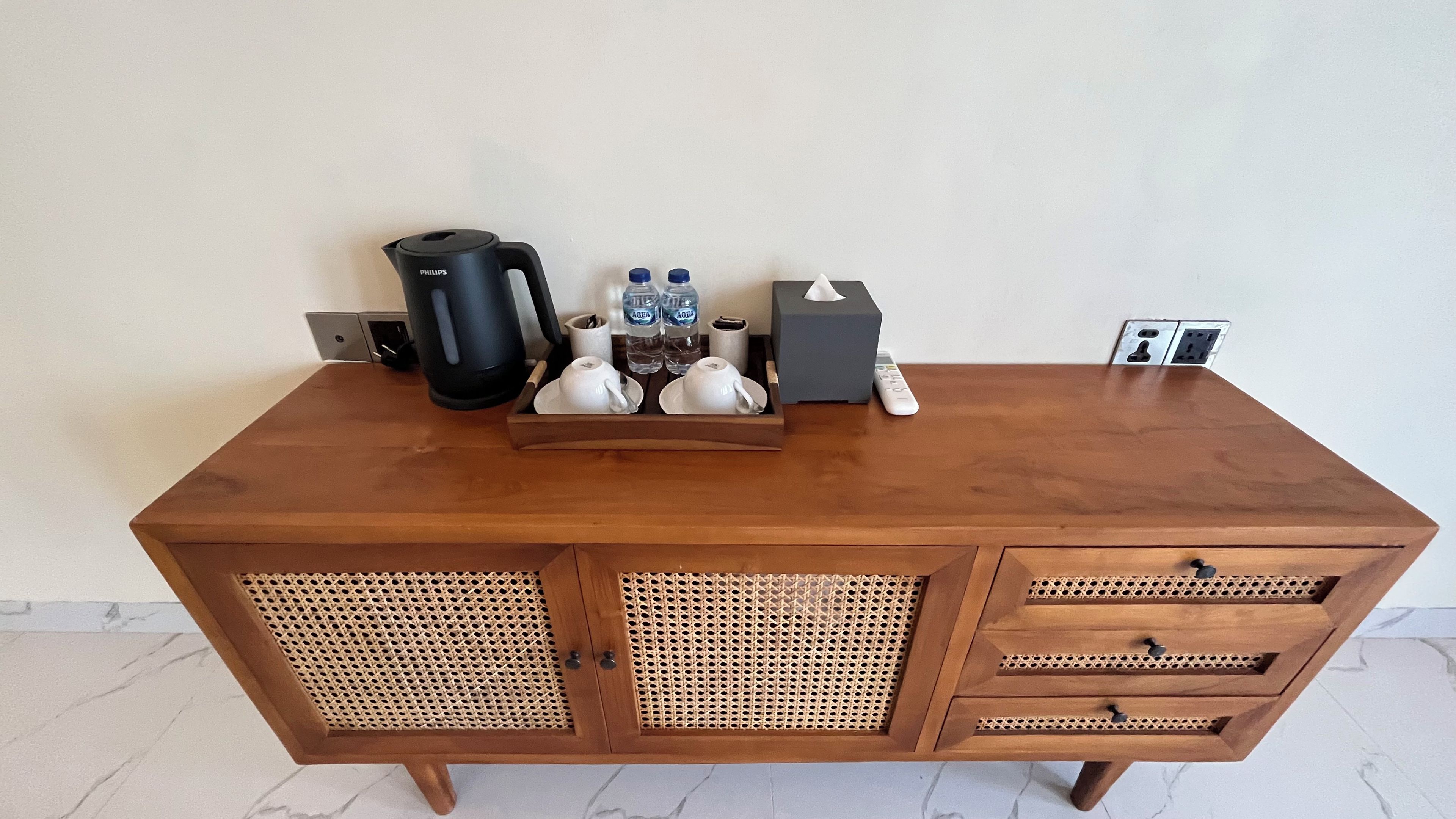 Mesa de madeira com cafeteira, garrafas de água, controle remoto e caixa de lenços.