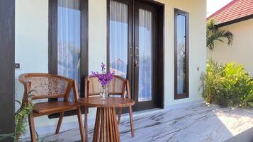A covered outdoor seating area with two wooden chairs and a table, a wooden ceiling, and a door with glass panels.