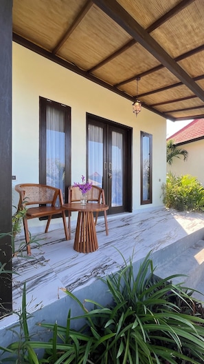 Un espacio al aire libre techado con dos sillas de madera y una mesa, techo de madera y una puerta con paneles de vidrio.