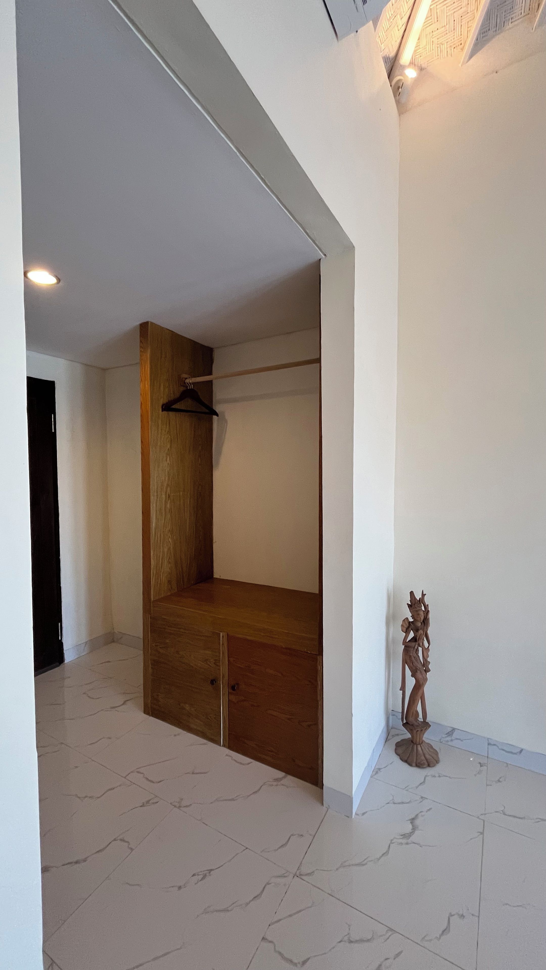 Een kamer met een houten garderobe, een kledingrek en een klein beeld op de vloer.