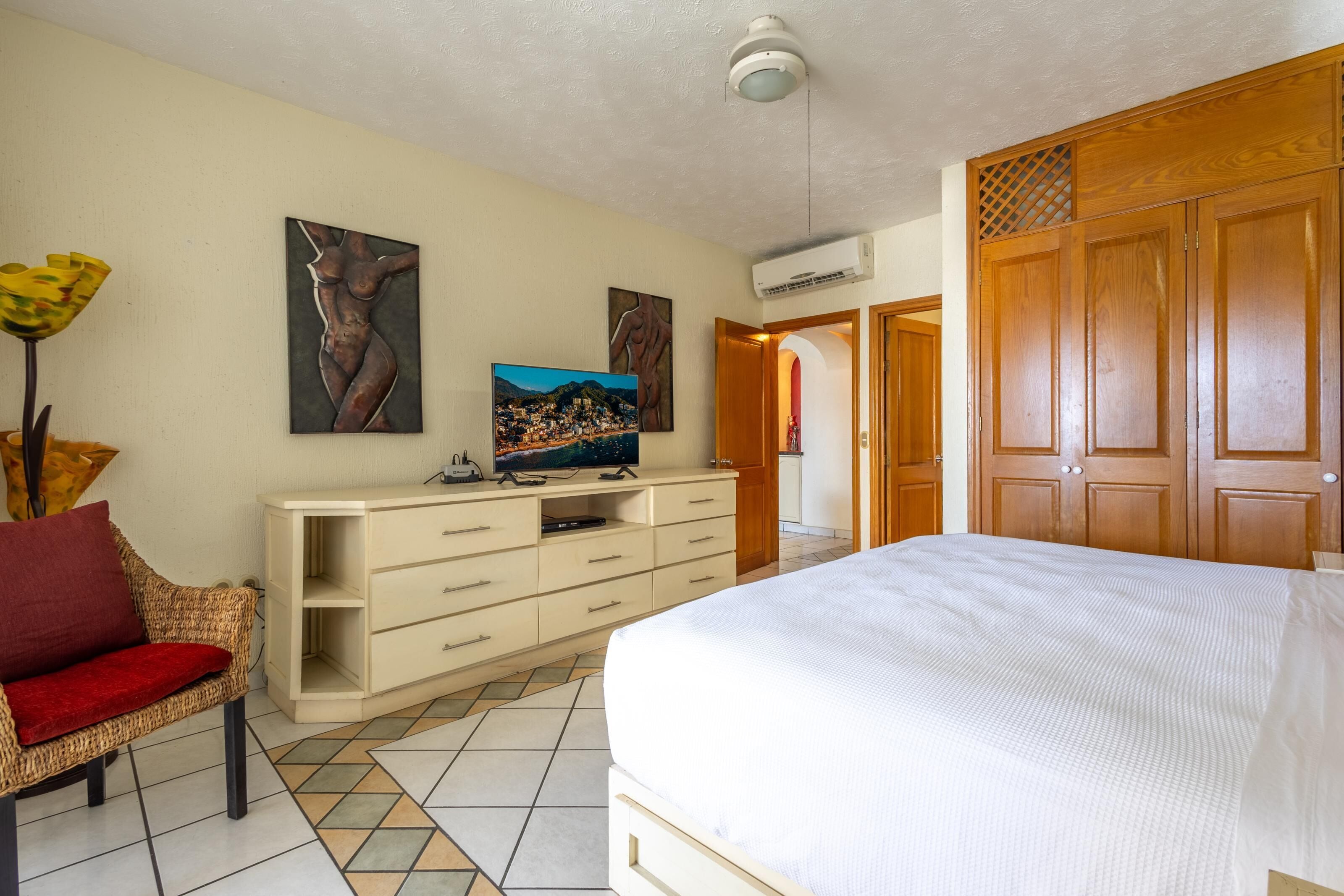 Ein Schlafzimmer mit einem Bett, einem Fernseher auf einer Kommode und Kunstwerken an der Wand.