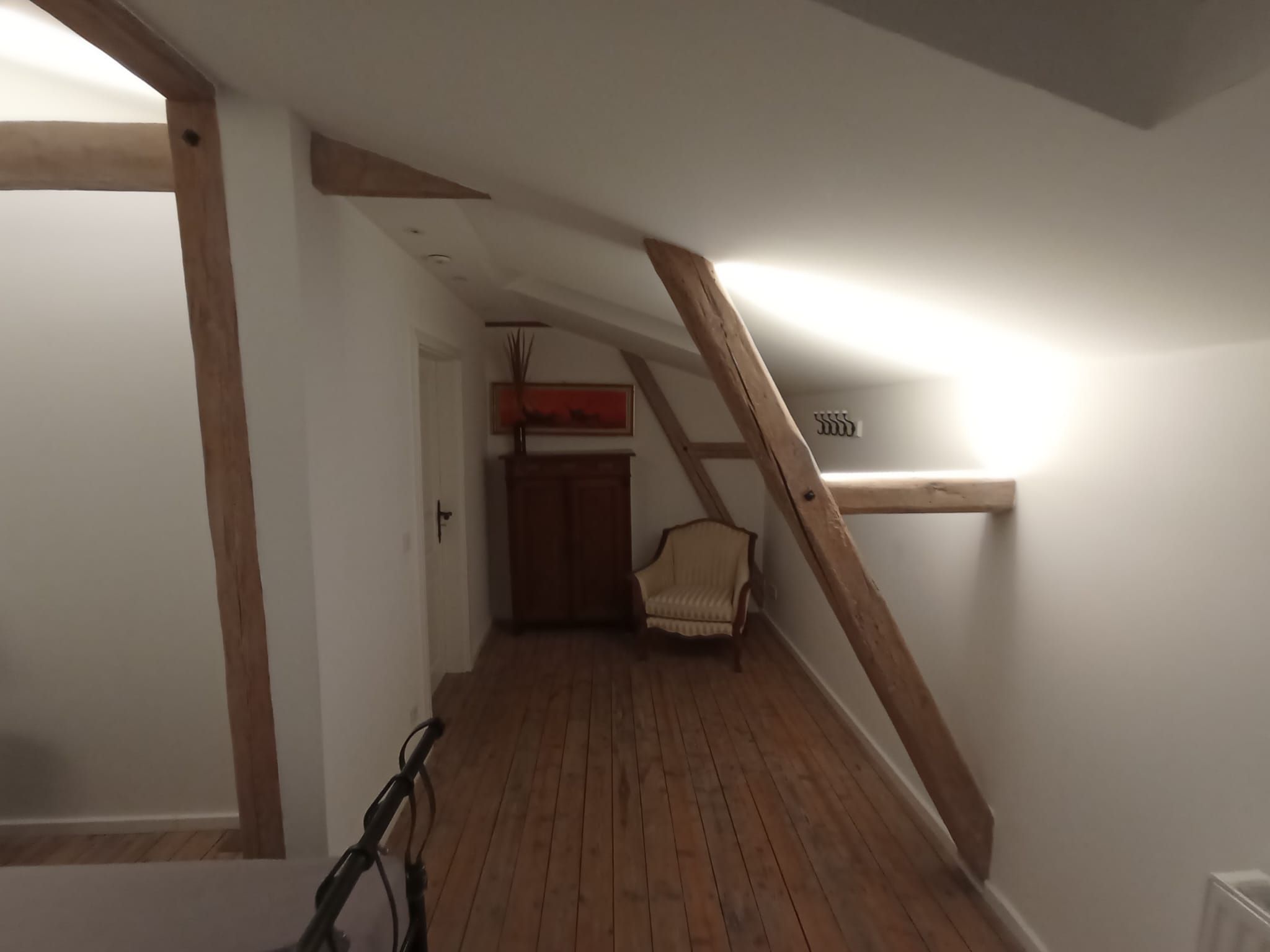 Ein schmaler Gang mit Holzbalken, einem Stuhl und einer Tür zu einem weiteren Raum.