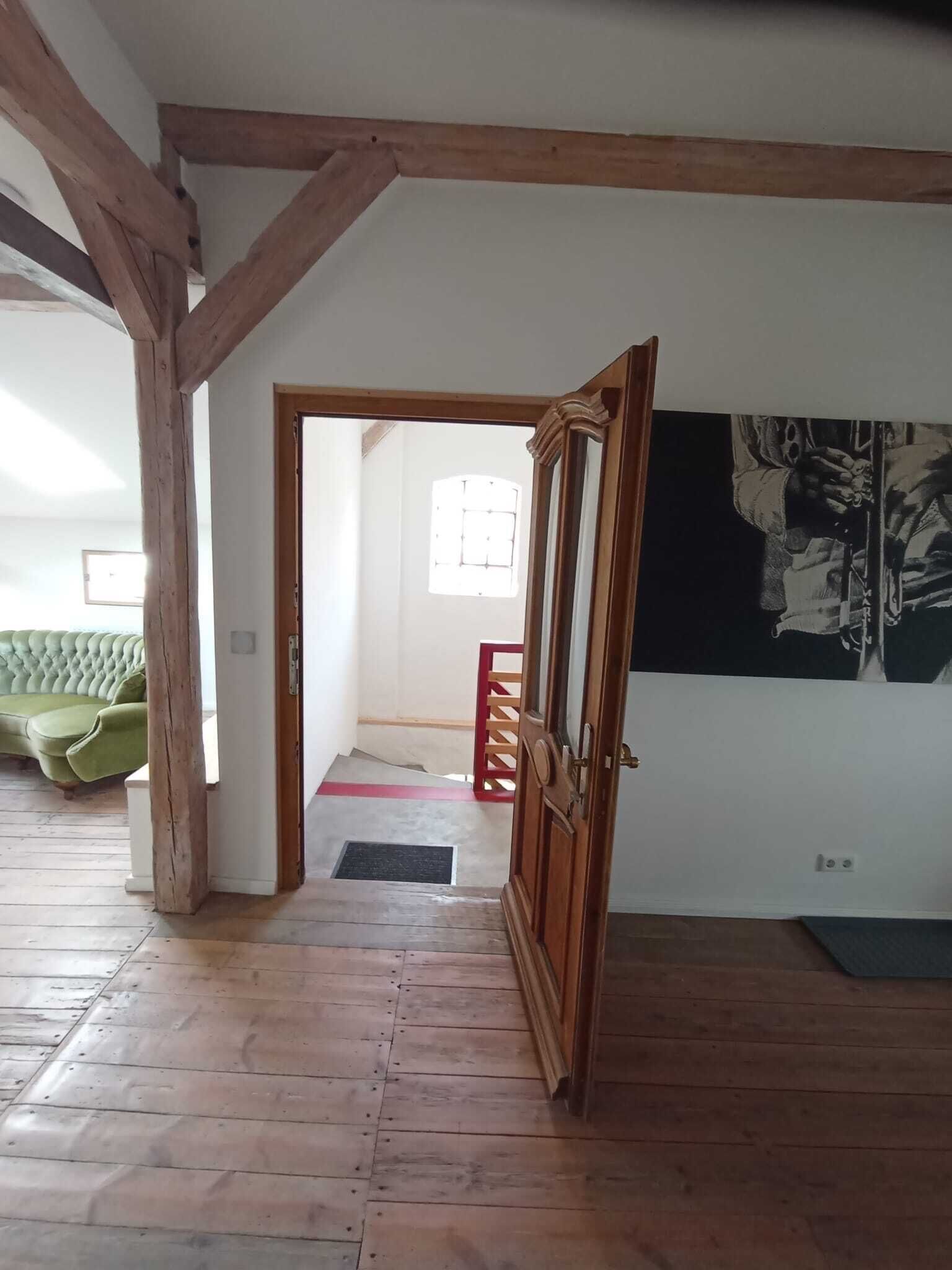 Ein Zimmer mit Holzbalken, einem grünen Sofa, einer Tür zu einem anderen Raum und einer Wand mit einem Schwarzweißkunstwerk.