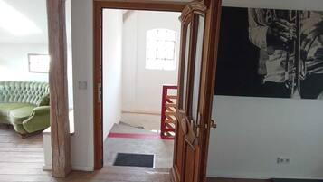 Ein Zimmer mit Holzbalken, einem grünen Sofa, einer Tür zu einem anderen Raum und einer Wand mit einem Schwarzweißkunstwerk.