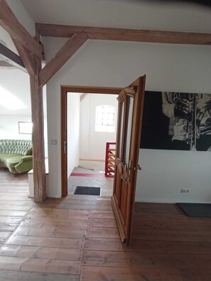 A room with wooden beams, a green sofa, a door leading to another room, and a wall with a black and white artwork. - Speicherstübchen (Schönberg)