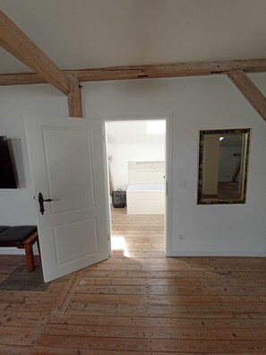 Una habitación con piso de madera, una puerta blanca y un espejo en la pared.