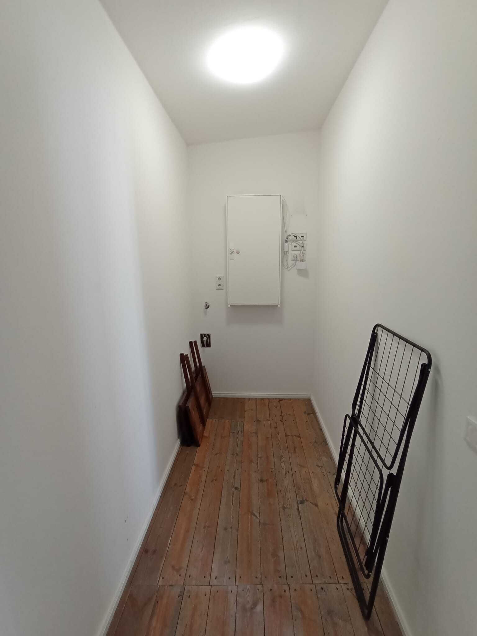 A narrow hallway with wooden flooring, white walls, and a white door at the end.