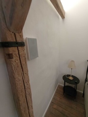 Un pasillo estrecho con vigas de madera, una pequeña mesa con una lámpara y un interruptor de luz en la pared.