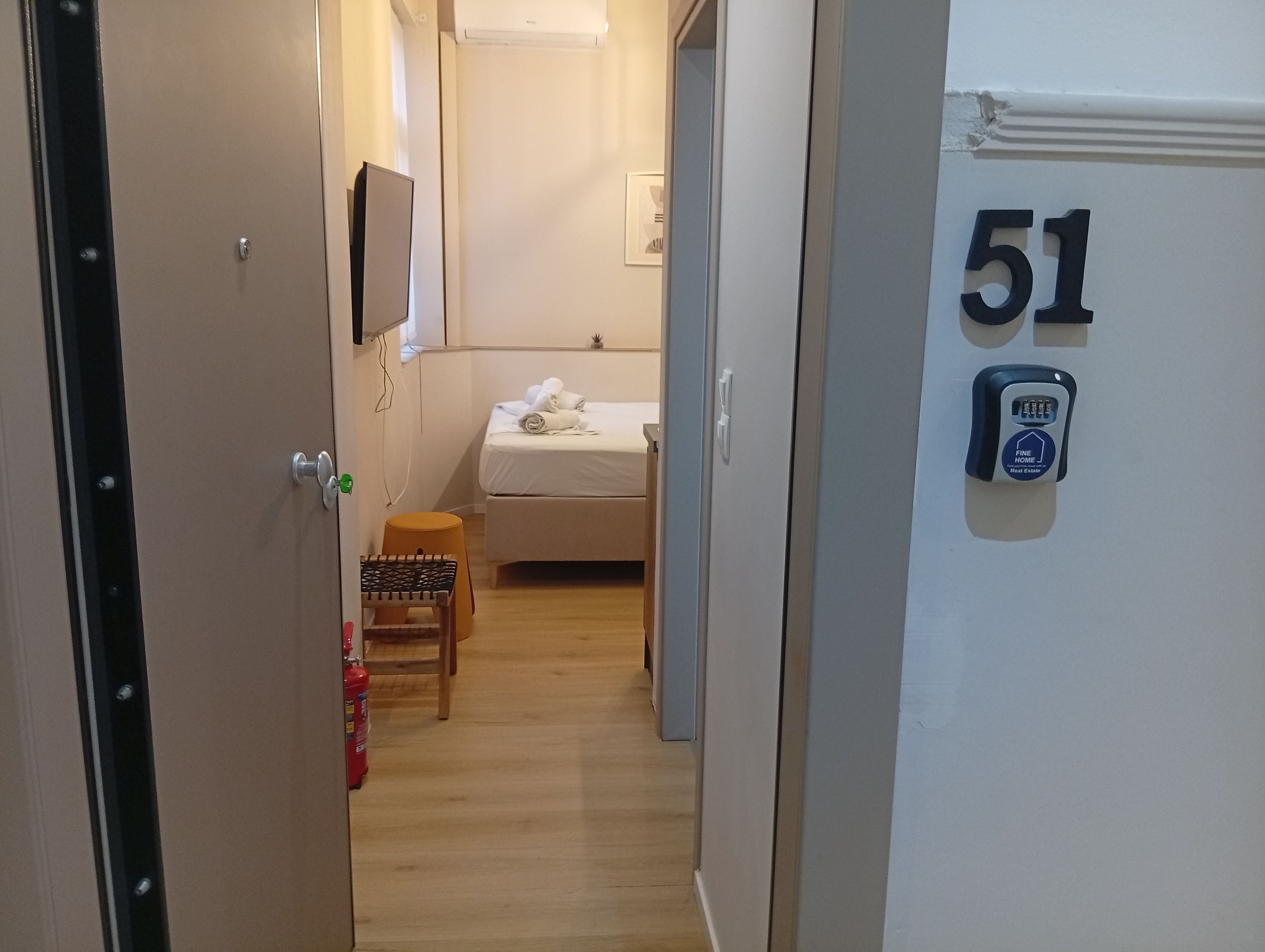 Habitación de hotel con cama, una mesita, una silla, extintor y una puerta con el número 51.