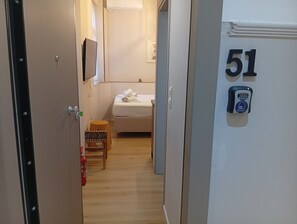 A hotel room with a bed, a small table, a chair, a fire extinguisher, and a door with the number 51. - Stylish City Center Apartment.Steps from Aristotelous (Thessaloniki)