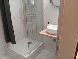 A modern bathroom with a glass-enclosed shower, a white sink, and a marble-tiled wall. - Stylish City Center Apartment.Steps from Aristotelous (Thessaloniki)