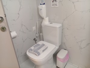 A bathroom with a toilet, a hand dryer, a trash bin, and a paper towel holder. - Stylish City Center Apartment.Steps from Aristotelous (Thessaloniki)
