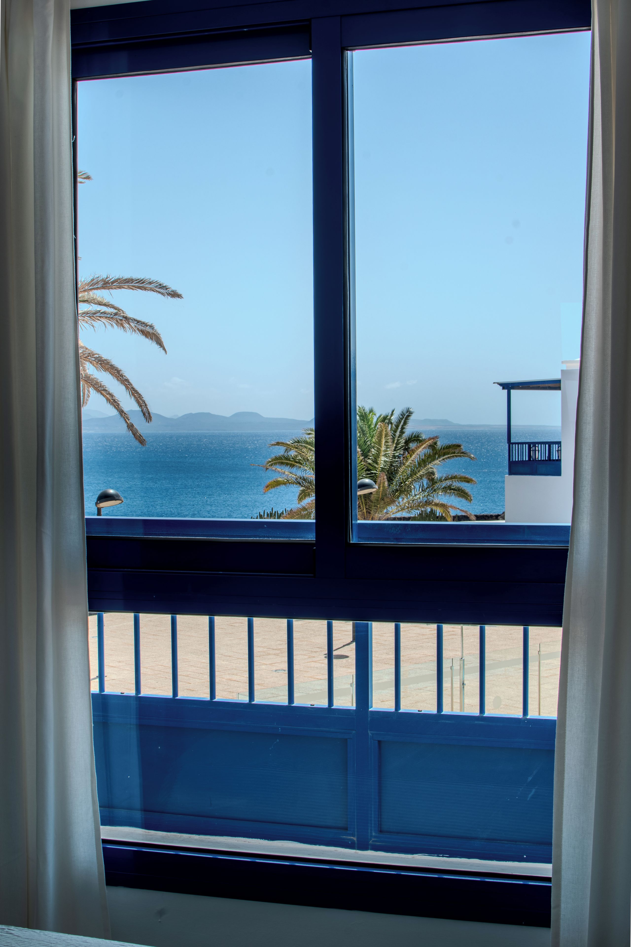 A window with a view of the sea and palm trees.