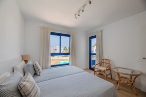 Ein Schlafzimmer mit einem Bett, einem Sessel, einem kleinen Tisch und Blick auf einen Pool.