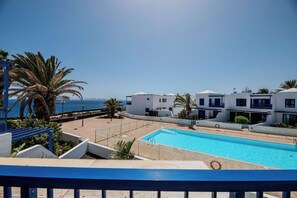 Ein Poolbereich mit freiem Blick auf das Meer, umgeben von weißen Gebäuden mit Balkonen und Palmen.