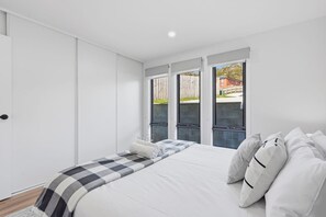 Ein Schlafzimmer mit einem Bett, einer karierten Decke und Blick durch große Fenster nach draußen.