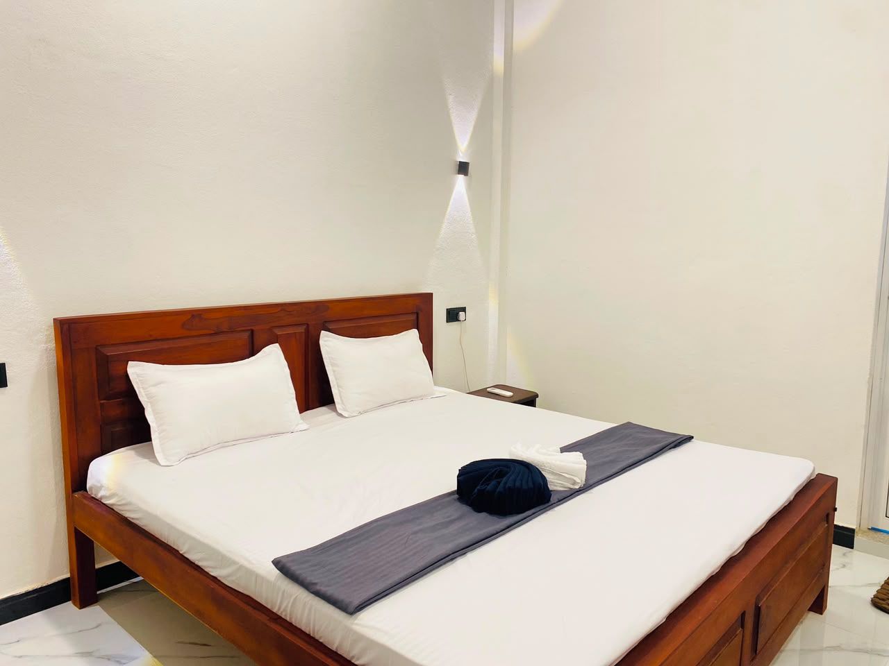 Cama bem arrumada com cabeceira de madeira, roupa de cama branca e toalha escura sobre a cama.