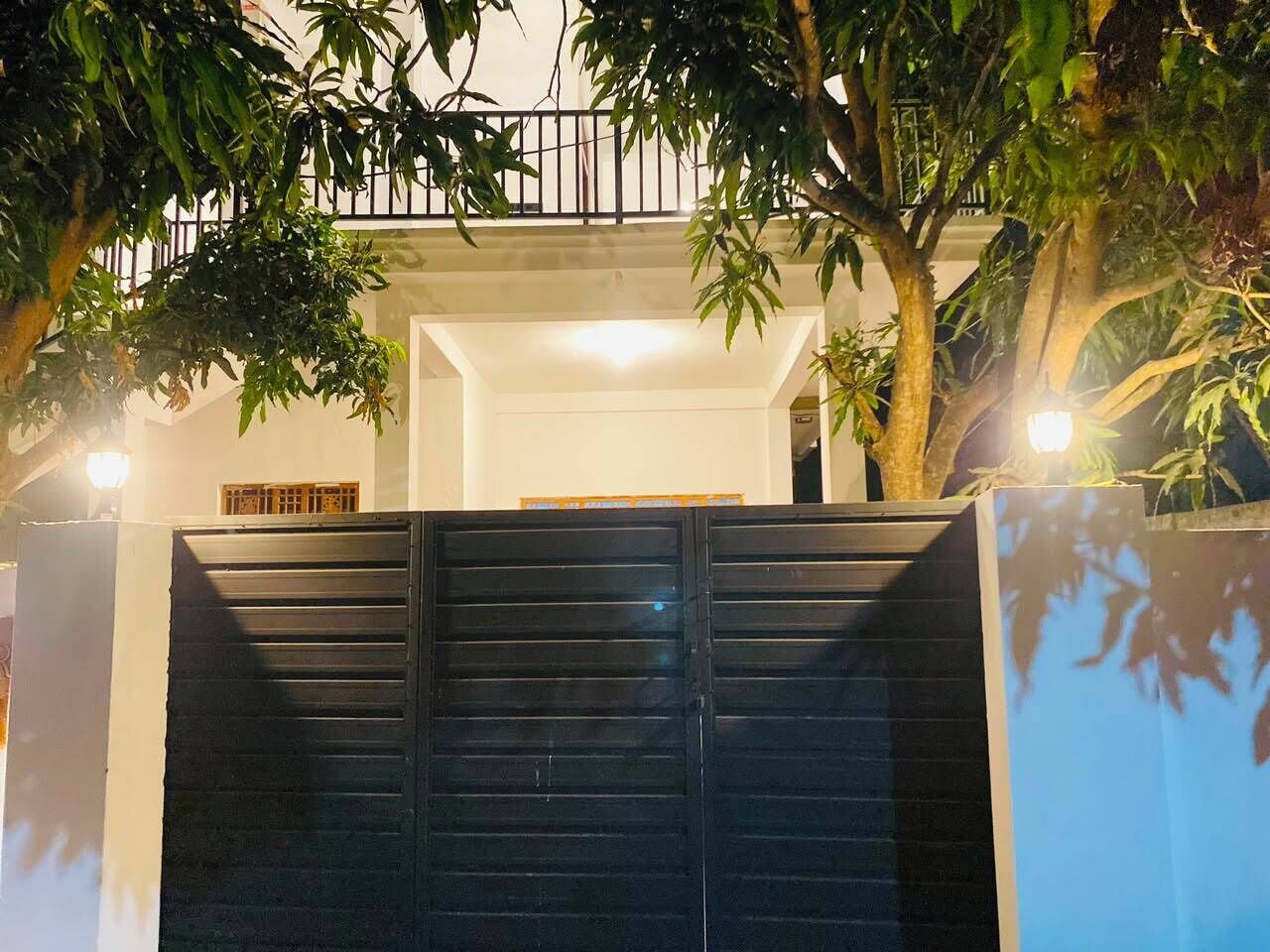 A gated entrance with a metal gate, a white wall, and a tree in the foreground.