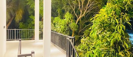 Ein moderner Innenraum mit einer Treppe zu einem Balkon, umgeben von üppigem Grün und einem weißen Geländer.