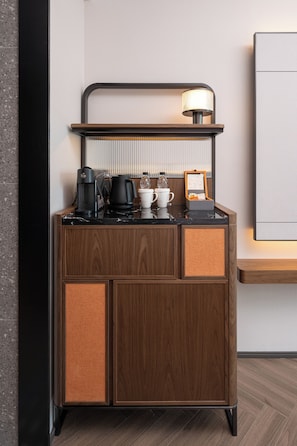 A compact, modern kitchenette with a coffee maker, kettle, and a small cabinet with a mirror.
