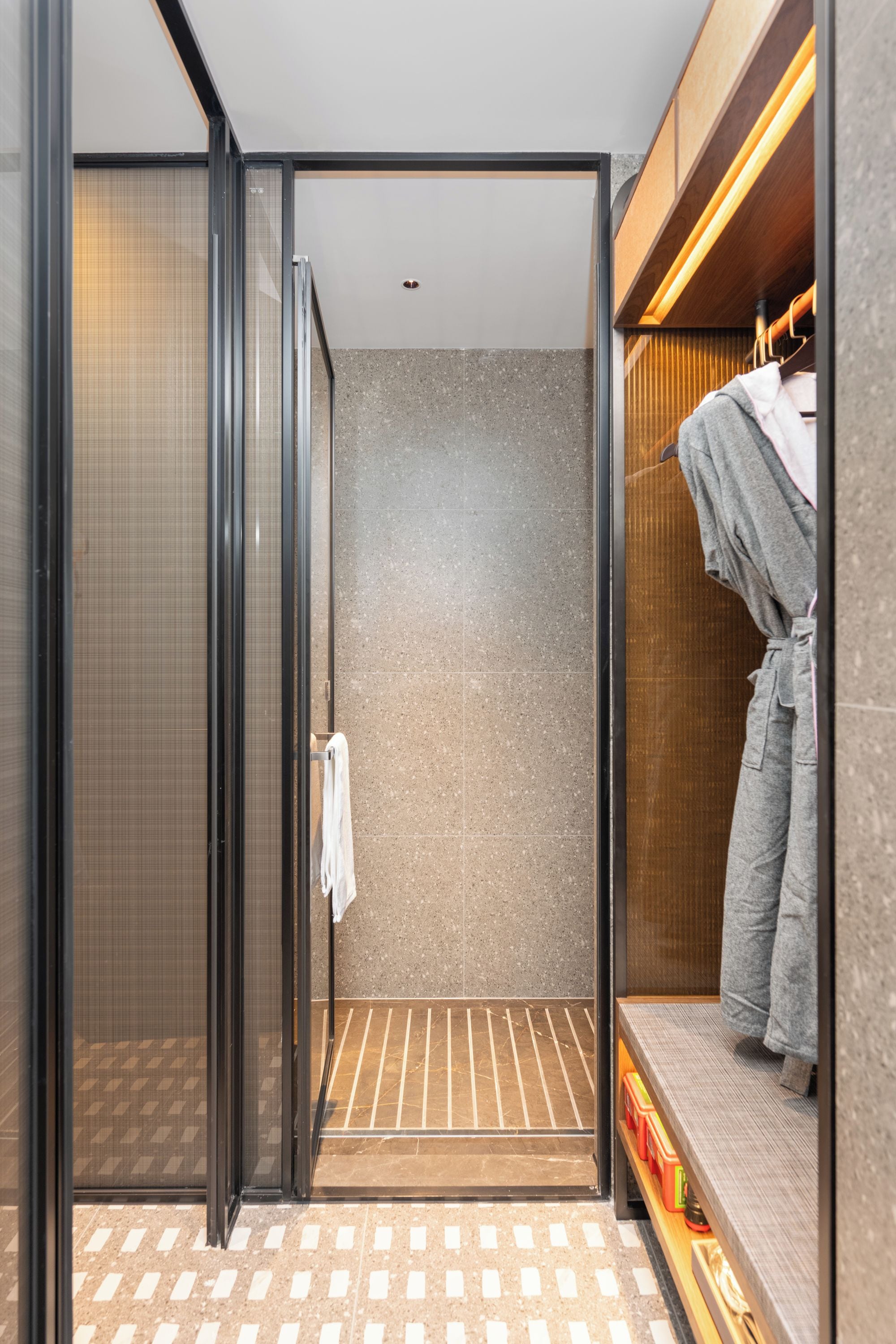 Une salle de bain moderne avec une douche à parois de verre, un porte-serviettes et un meuble-lavabo en bois sur lequel est suspendue une serviette.