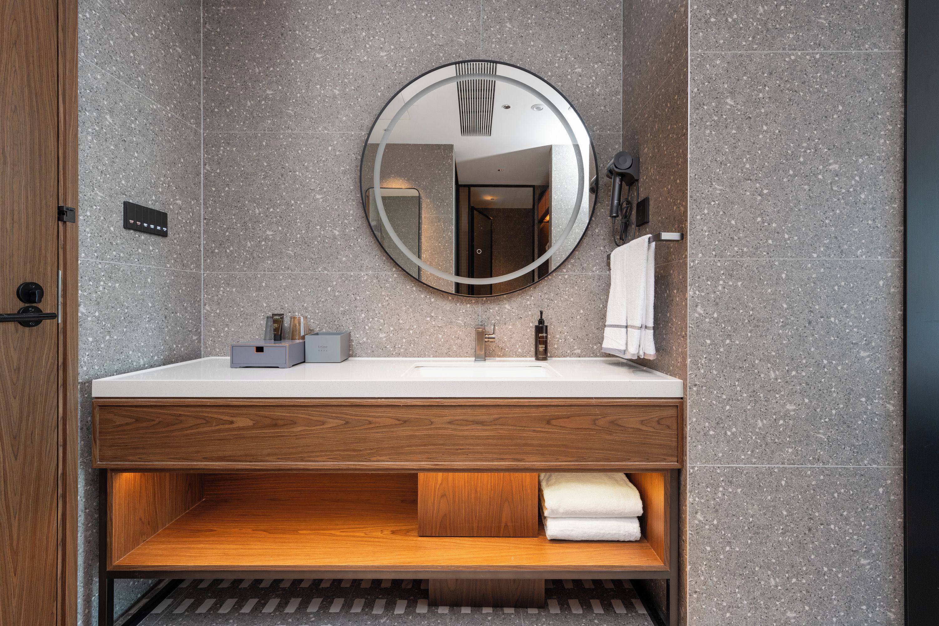 A modern bathroom with a wooden vanity, a round mirror, and a towel rack.