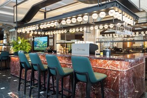 A bar area with a marble counter, bar stools, and a television screen.