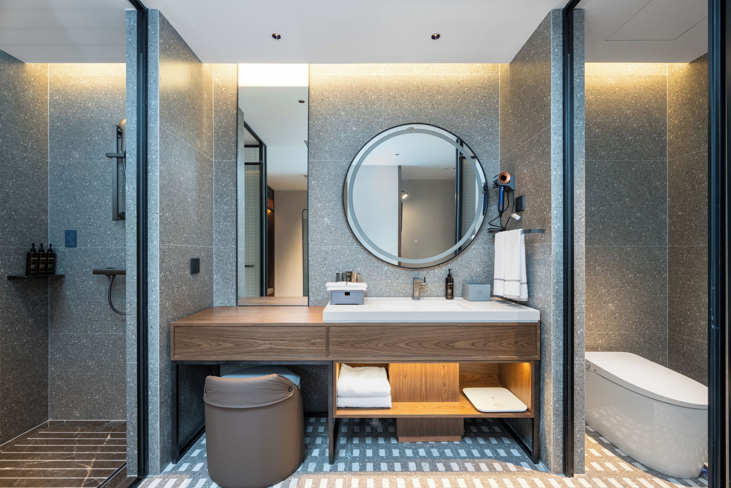 A modern bathroom with a wooden vanity, a round mirror, and a built-in toilet.