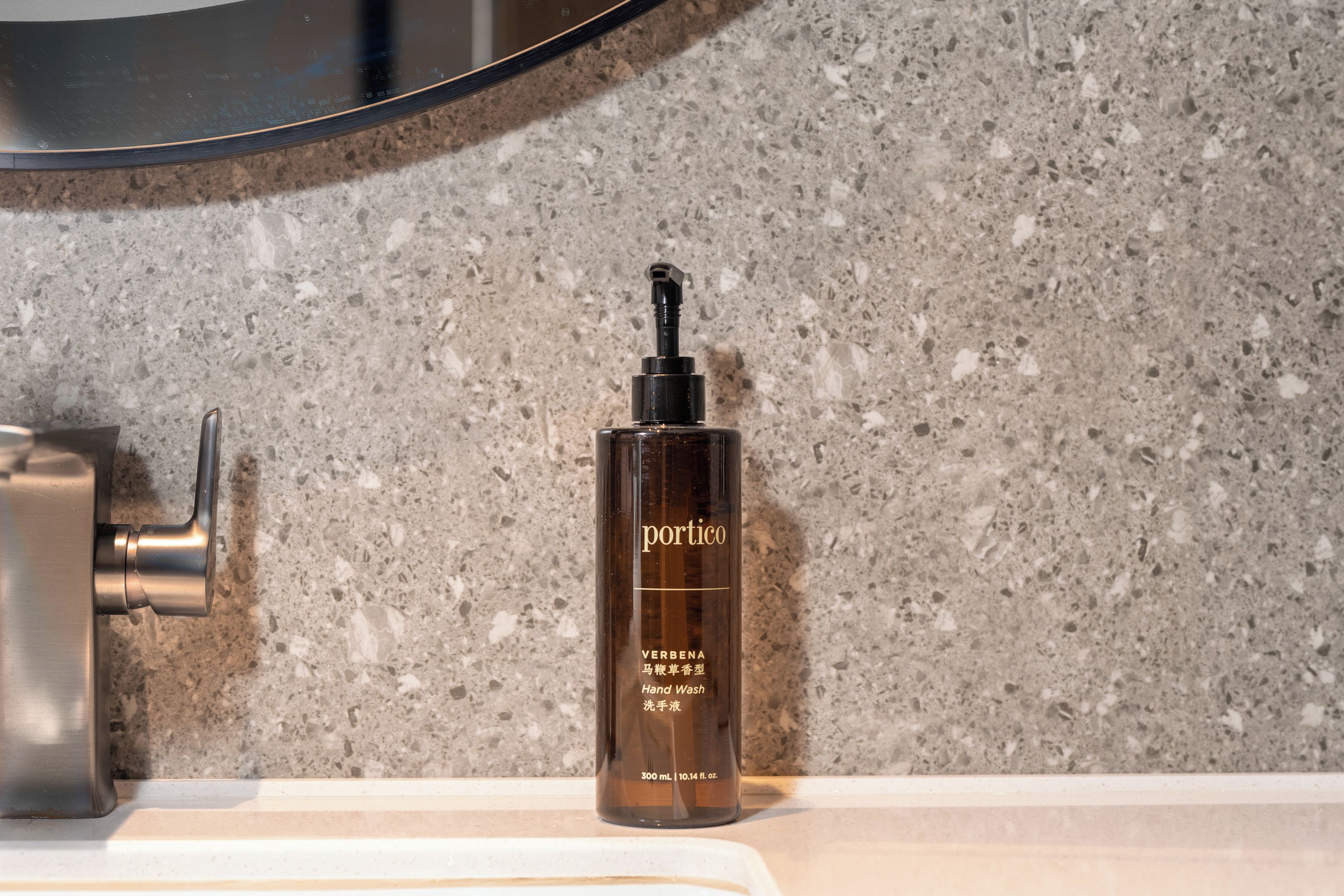 A bottle of Portico hand wash on a countertop with a speckled backsplash.