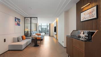 A modern hotel room with a sofa, dining table, and kitchenette.