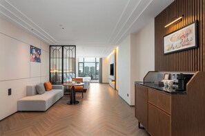 A modern hotel room with a sofa, dining table, and kitchenette.