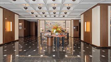 A spacious lobby with a polished marble floor, a central round table with a floral arrangement, and traditional wooden paneling on the walls.