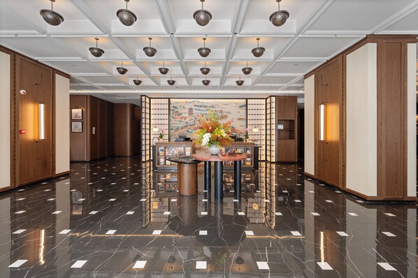 A spacious lobby with a polished marble floor, a central round table with a floral arrangement, and traditional wooden paneling on the walls.