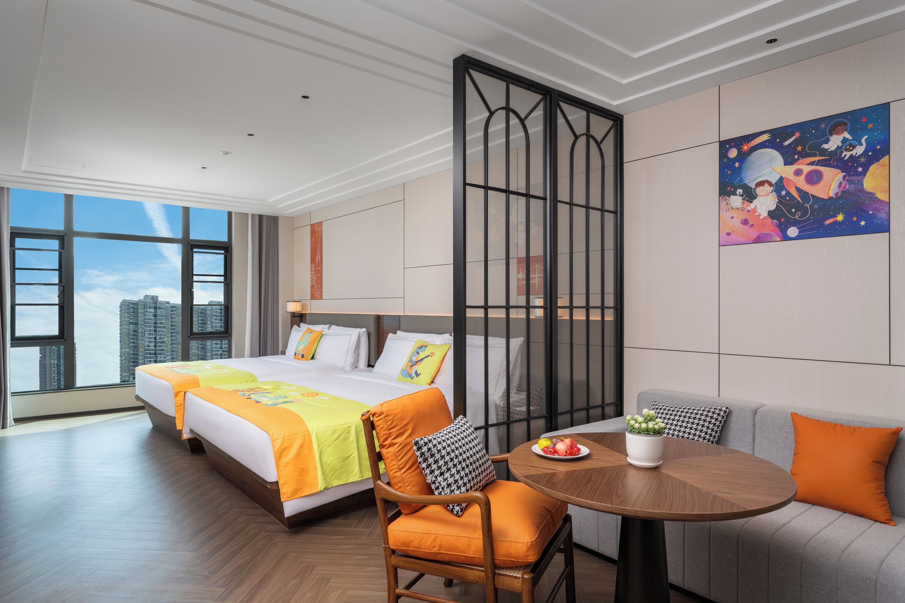 A hotel room with a large bed, a sofa, a dining table, and a city view.