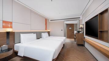 A modern hotel room with a large bed, a TV, a desk, and a bathroom visible through an open door.