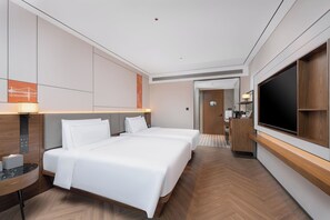 A modern hotel room with a large bed, a TV, a desk, and a bathroom visible through an open door.