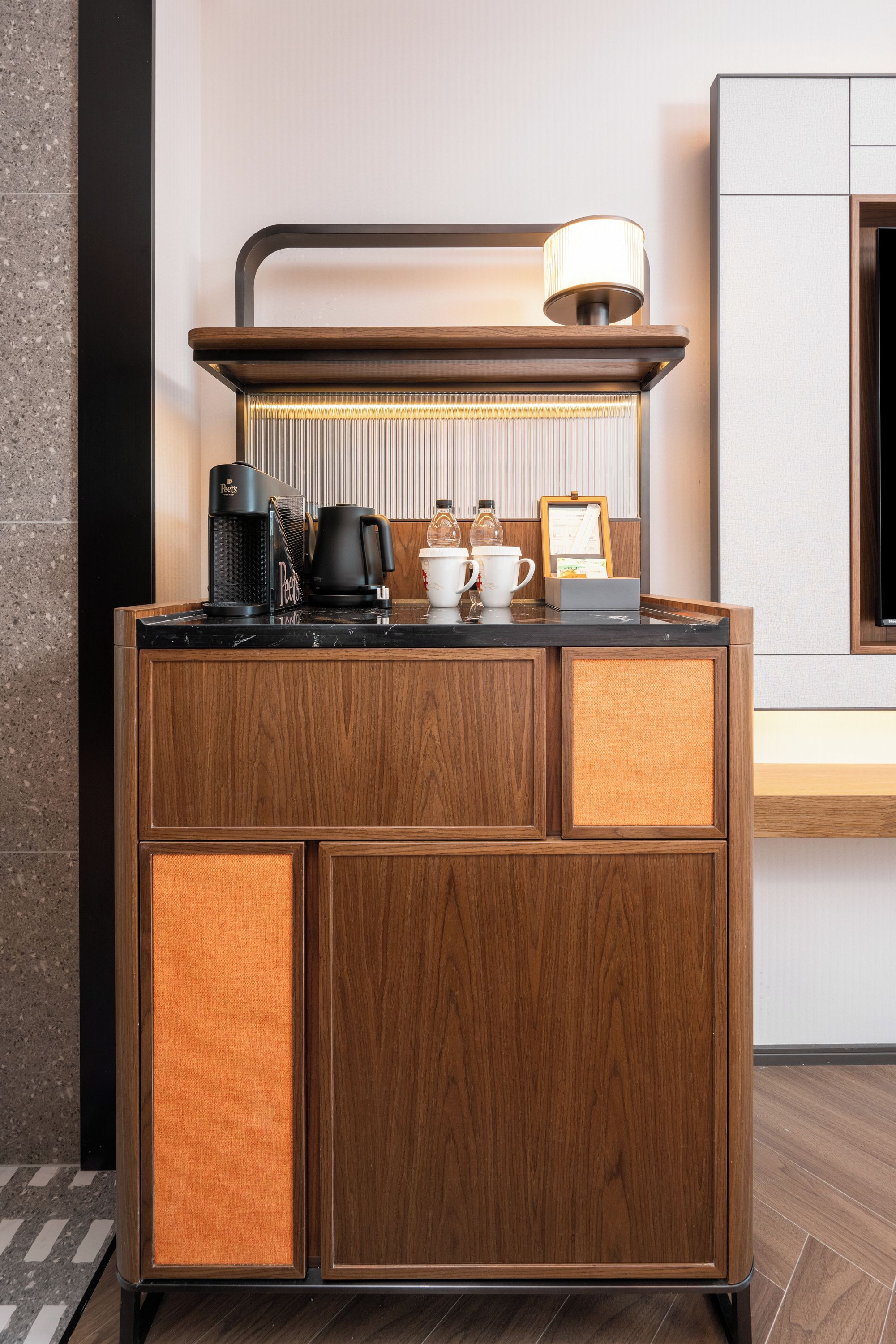 A wooden minibar with a coffee maker, a kettle, and a lamp.