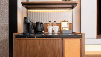 A wooden minibar with a coffee maker, a kettle, and a lamp.