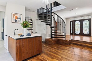 A modern interior with a wooden floor, a white reception desk, a black spiral staircase, and a door with stained glass. - ACL Weekend | Sleeps 22 | Pool + Hot Tub + Sauna | Game Room | The Reset Estate (Austin)