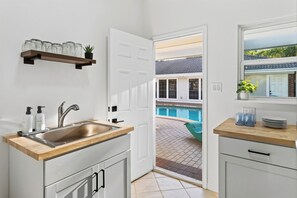Eine kompakte Küche mit Spüle, Holz Arbeitsplatte und Blick auf einen Swimmingpool durch eine offene Tür.