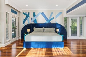 Ein Schlafzimmer mit einem großen Bett, einer blauen Akzentwand und Blick ins Freie durch die Fenster.
