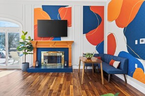 Ein modernes Wohnzimmer mit Kamin, einem flachbildfernseher darüber, einem blauen Sofa und Holzboden.