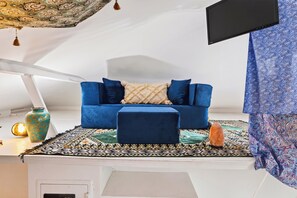 A blue sofa with a patterned throw, a small ottoman, and a decorative vase on a patterned rug. - ACL Weekend | Sleeps 22 | Pool + Hot Tub + Sauna | Game Room | The Reset Estate (Austin)